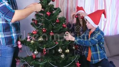 爸爸、妈妈和儿子戴着圣诞帽，用珠子和球装饰圣诞树。 家准备<strong>平安</strong>夜..